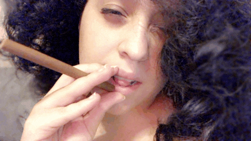 a woman with curly hair is smoking a cigar with her eyes closed