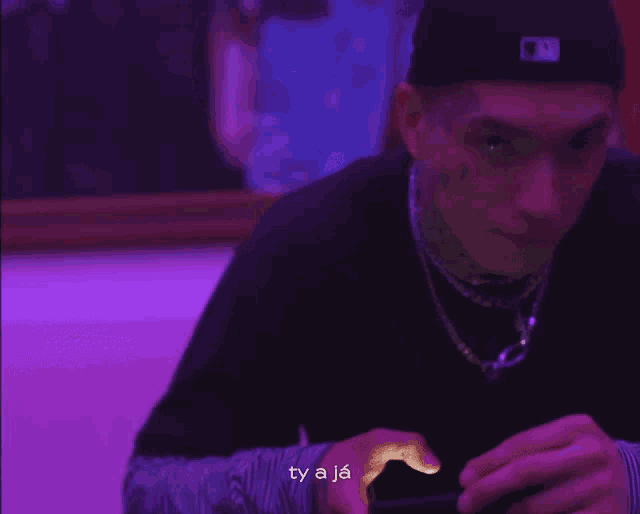 a man wearing a hat and a necklace is looking at his phone