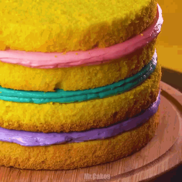 a yellow cake with pink blue and purple frosting sits on a wooden cutting board
