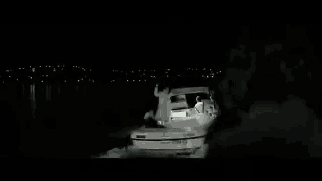 a man is standing on a dock at night looking at a boat .