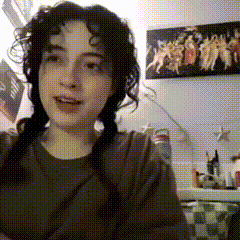 a girl with pigtails is smiling in front of a wall with a painting of angels on it