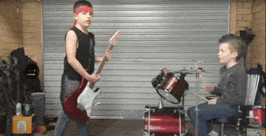 a boy playing a guitar and another boy playing drums in a garage