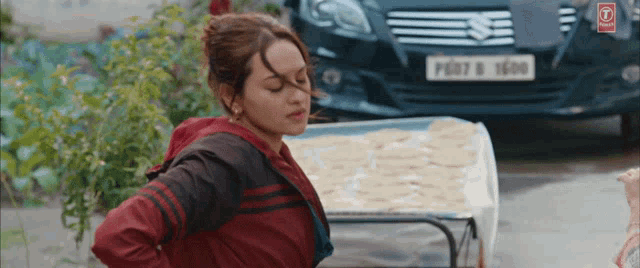 a woman in a red jacket stands in front of a suzuki