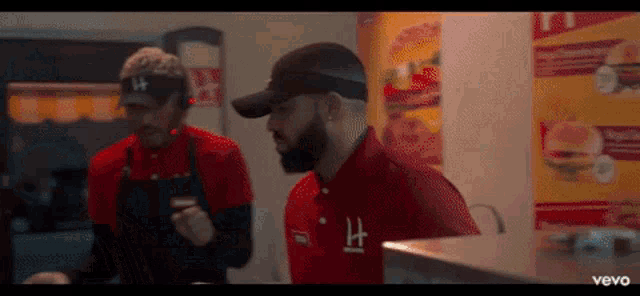 a man in a red shirt with the letter h on it is standing next to another man