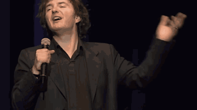 a man in a suit is singing into a microphone with his hands in the air