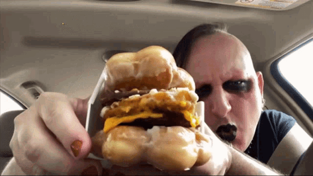 a man eating a hamburger in a car with a visor that says ' warning ' on it