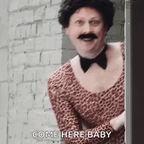a man with a wig and mustache is peeking out from behind a door and says `` come here baby '' .
