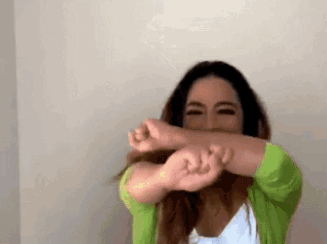 a woman wearing a green sweater is covering her face with her hands .
