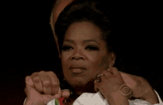 oprah winfrey is sitting in front of a microphone holding her hands together and making a face .