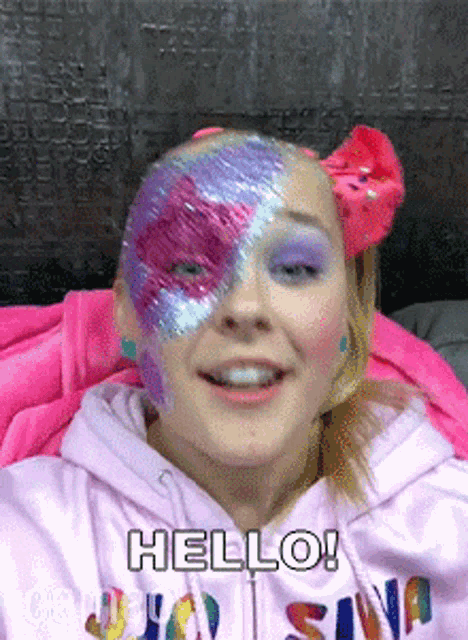 a girl with glitter paint on her face is smiling and saying hello