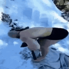 a man without a shirt is kneeling down in the snow with a shovel .