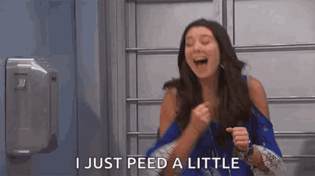 a woman is laughing while standing in front of a hand sanitizer dispenser in a bathroom .