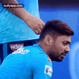 a man in a blue shirt is getting his hair braided by another man in a blue shirt .