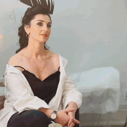 a woman wearing a black top and a white shirt is sitting with her hands folded
