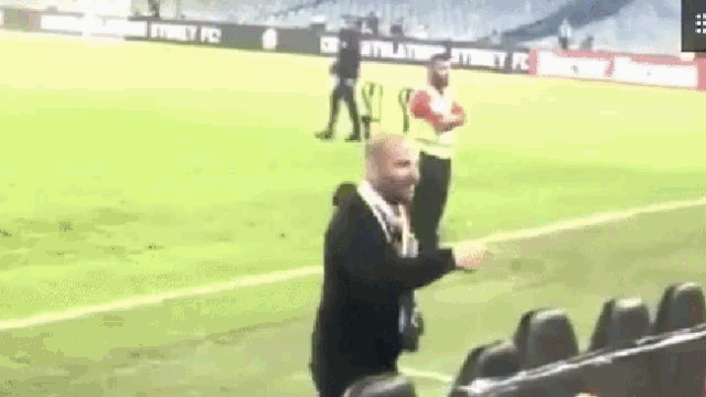 a man in a suit is standing on a soccer field talking on a cell phone .