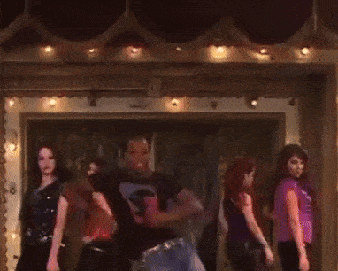 a group of people are dancing in a dark room with a man wearing a black shirt with the letter s on it