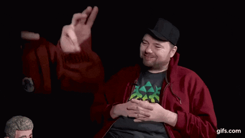 a man wearing a red jacket and a black hat is smiling and pointing