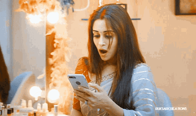a woman is looking at her phone in front of a mirror that says ruksarcreations on it