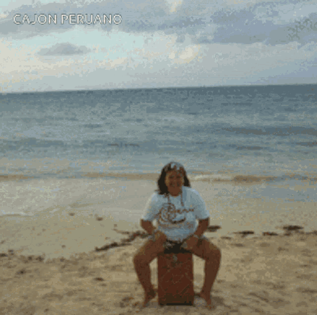 a woman sits on a red box on the beach with cajon peruano written on the top