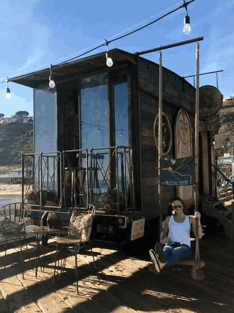 a woman sits on a swing in front of a building that has a sign on it that says pacific coast