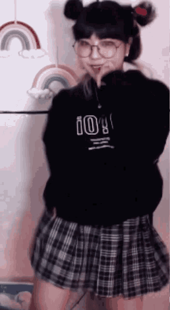 a girl wearing a black sweater and a plaid skirt is dancing in front of a rainbow .