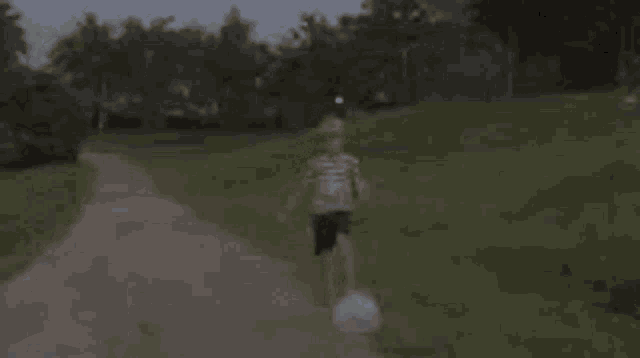 a young boy is playing with a soccer ball on a dirt road .