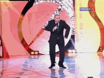 a man in a suit and tie stands on a stage with a microphone and a sign that says " russia "