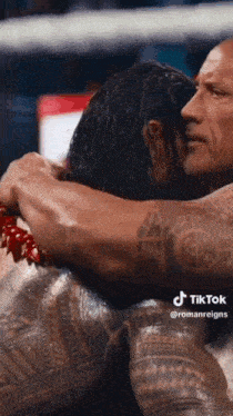 roman reigns and the rock hugging each other in a wrestling ring