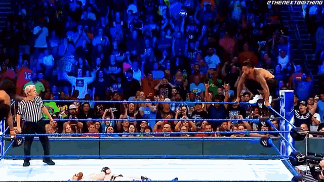 a wrestler is jumping over a referee in a wrestling ring with the next big thing written on the bottom right