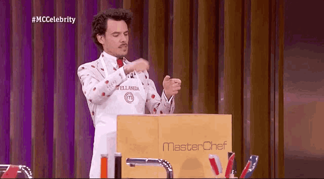 a man in an apron is standing at a podium with a master chef logo on it .
