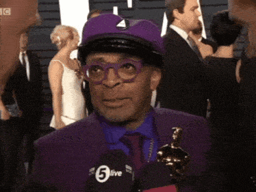 a man in a purple suit is talking into a microphone that says 5live