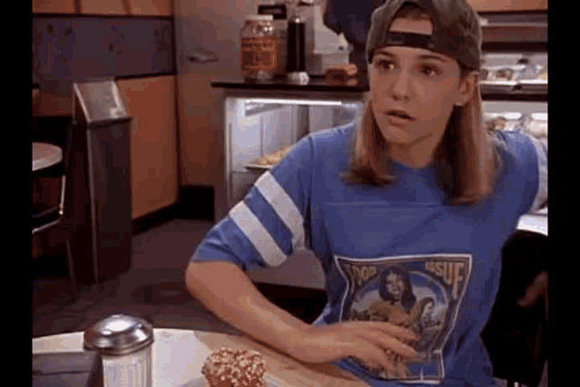 a woman wearing a baseball cap and a blue shirt is sitting at a table with a muffin .