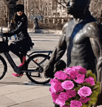 a statue of a man holding a bouquet of pink roses next to a woman riding a bike