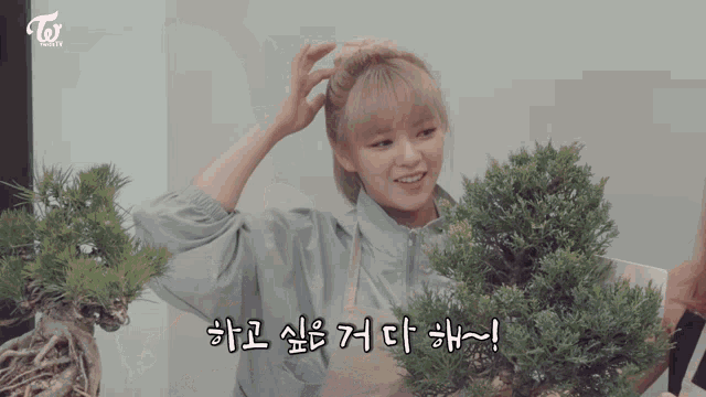 a woman is holding a bonsai tree with a twice logo in the background