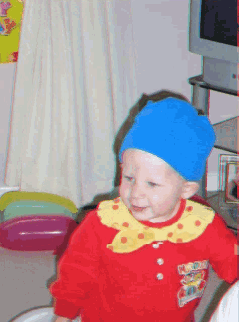 a baby wearing a blue hat and a red sweater with a yellow collar