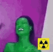 a woman with green hair is laughing in front of a purple wall with a yellow nuclear symbol .