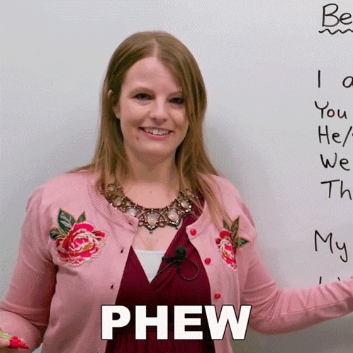 a woman in a pink cardigan stands in front of a whiteboard with phew written on it