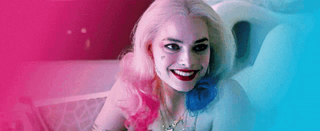 harley quinn is smiling while sitting in a bathtub .