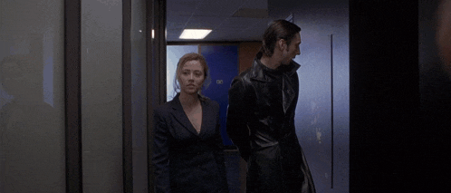 a man and a woman are walking in a hallway with a blue door that says exit