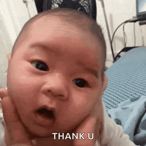 a baby with a surprised look on his face is being held by a person and the baby is saying thank u