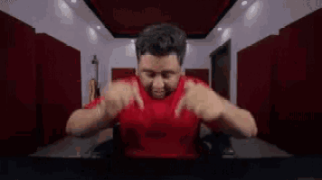 a man in a red shirt is sitting at a table in a room .
