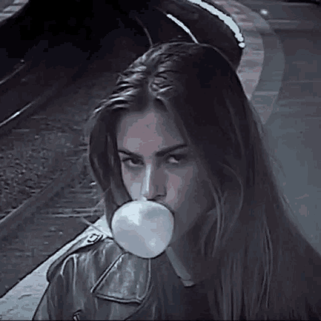 a woman is blowing a bubble of gum in front of a train track .