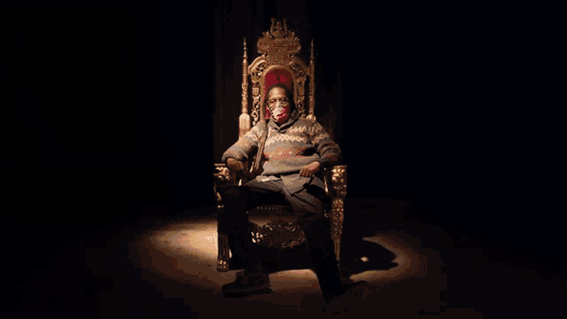 a man wearing a mask is sitting on a gold throne