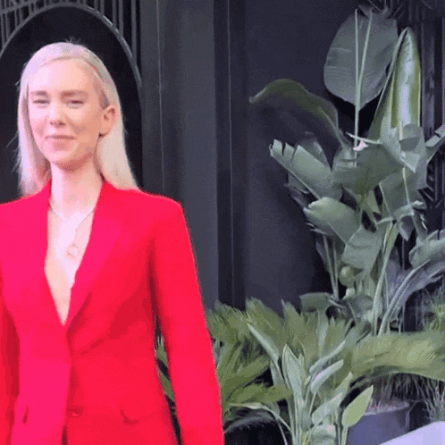 a woman in a red suit is smiling in front of a plant