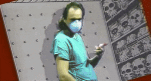 a man wearing a surgical mask stands in front of a wall with skulls on it