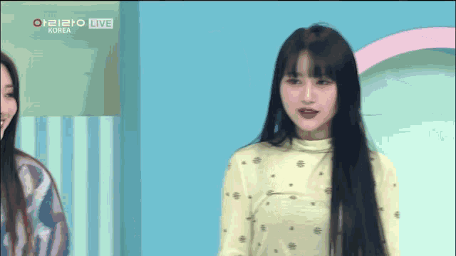 a woman with long black hair is standing in front of a blue wall with the word korea on it