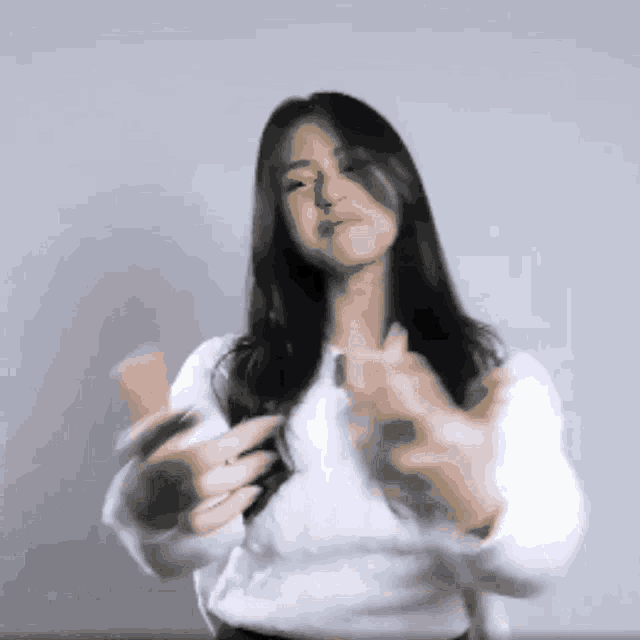 a woman in a white sweater is clapping her hands in front of her face