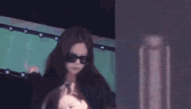 a woman wearing sunglasses is standing next to another woman in front of a screen .