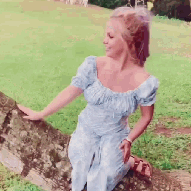 a woman in a blue dress is kneeling on a tree branch