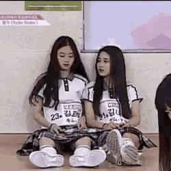 two girls are sitting next to each other on the floor in a classroom .